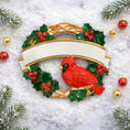 Load image into Gallery viewer, Personalized cardinal wreath ornament featuring a vibrant red cardinal bird surrounded by green holly leaves and red berries. Designed with a smooth glossy finish and a raised 3D front with a flat back for easy hanging. Includes free handwritten personalization with one name and year displayed on the banner at the top. Styled in a warm festive holiday setting with soft Christmas lights candy details and seasonal decor. A meaningful Christmas tree ornament symbolizing remembrance love and connection perfect