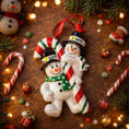Load image into Gallery viewer, Two snowman ornaments with candy canes on a wooden surface with Christmas decorations.