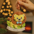 Load image into Gallery viewer, Lion themed Christmas ornament designed with a playful and colorful style, perfect for kids and animal lovers. This ornament features a lion character standing on a grassy base with a glossy finish and cheerful details. The design includes a personalization option, allowing a custom name and year to be added, making it a meaningful keepsake for children or family holiday traditions. Ideal for Christmas trees, nursery decor, or as a unique personalized gift for animal themed celebrations.