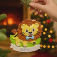 Load image into Gallery viewer, Lion themed Christmas ornament designed with a playful and colorful style, perfect for kids and animal lovers. This ornament features a lion character standing on a grassy base with a glossy finish and cheerful details. The design includes a personalization option, allowing a custom name and year to be added, making it a meaningful keepsake for children or family holiday traditions. Ideal for Christmas trees, nursery decor, or as a unique personalized gift for animal themed celebrations.
