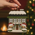 Load image into Gallery viewer, Personalized Christmas house ornament featuring a cozy winter home decorated with snow, wreaths, garlands, and festive details. Two smiling characters wearing Santa hats peek from the front, each customizable with a name, while the roof displays a year or family name. Designed with a detailed 3D raised front and smooth finish, this ornament is perfect for Christmas tree decor, family keepsakes, new home celebrations, and holiday gifting.