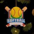 Load image into Gallery viewer, Personalized softball Christmas ornament featuring a yellow softball with stitched details and crossed bats design on a shield style background, customizable name area on the front banner and customizable year area on the softball, glossy finish with raised 3D front details and flat 2D back, white hanging ribbon, displayed on a snowy softball field themed holiday background with pine branches and festive decorations.