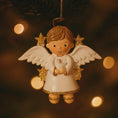 Load image into Gallery viewer, Angel ornament holding a dove against a warm, blurred lights background