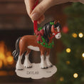 Load image into Gallery viewer, Horse Christmas ornament with a wreath and bow, held by a hand against a festive background.