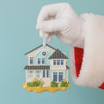 Load image into Gallery viewer, Hand wearing a white glove holding a miniature house ornament against a light blue background