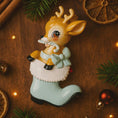 Load image into Gallery viewer, A glossy resin baby deer ornament features a cute fawn character sitting inside a soft pastel blue winter boot, holding a striped candy cane, with gentle antler details, smooth painted cartoon style finish, soft holiday lighting and blurred festive background, handwritten personalization showing the baby name on the boot and the year or Baby’s First Christmas text below, designed as a mostly 2D ornament with raised 3D details on the front only.