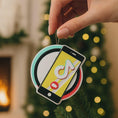 Load image into Gallery viewer, Decorative ornament with smartphone and music note design, held against a festive background.