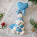 Load image into Gallery viewer, Decorative snowman ornament with blue heart and bow on a snowy background