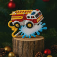 Load image into Gallery viewer, Colorful toy fire truck ornament on a wooden stump with Christmas decorations in the background.