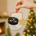 Load image into Gallery viewer, Hand holding a hockey-themed Christmas ornament with a star against a festive background.
