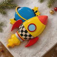 Load image into Gallery viewer, Colorful rocket-shaped ornament on a textured surface with Christmas decorations.