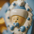 Load image into Gallery viewer, Close-up of a ornament with a blue hat and mittens on a blurred background