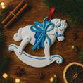 Load image into Gallery viewer, Decorative rocking horse ornament with a blue bow on a wooden surface with Christmas decorations.