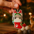 Load image into Gallery viewer, Christmas ornament of a cat in a stocking with reindeer antlers held by a hand against a festive background.