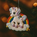 Load image into Gallery viewer, Unicorn ornament with rainbow on a blurred Christmas tree background