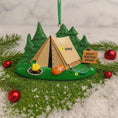 Load image into Gallery viewer, Camping-themed ornament with a tent, fire, and sign on a green base with trees and red ornaments.