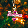 Load image into Gallery viewer, Personalized Babysitter Christmas ornament featuring a detailed raised 3D front design with glitter pink lettering and a charming girl figure. Custom name is added on the shirt and year is written on the hanging heart charm. Bright pink and white holiday colors stand out beautifully on the tree. Flat 2D back for easy hanging. Perfect keepsake gift for babysitter appreciation, nanny thank you present, childcare provider Christmas decor.