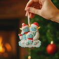 Load image into Gallery viewer, Hand holding a Christmas ornament with three cartoon characters in front of a blurred Christmas tree and fireplace.