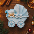 Load image into Gallery viewer, Personalized baby boy Christmas ornament featuring a light blue stroller with glitter details and a smiling baby wearing a blue nightcap. Custom name appears on the top and year on the bottom, making it a perfect Baby’s First Christmas keepsake. This blue resin holiday ornament is ideal for newborn boys, baby shower gifts, and celebrating a special first Christmas memory.