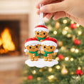 Load image into Gallery viewer, Three gingerbread men Christmas ornaments with Santa hats held by a hand against a festive background.