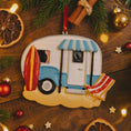 Load image into Gallery viewer, Decorative ornament of a camper with a surfboard and beach chair on a wooden surface with Christmas decorations.