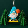 Load image into Gallery viewer, Personalized basketball gnome Christmas ornament featuring a cute blue gnome character holding a basketball, customizable name area on the hat and customizable year area on the base, glossy finish with raised 3D front details and flat 2D back, white hanging ribbon, displayed on a snowy holiday background with pine branches and festive decorations.