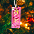 Load image into Gallery viewer, A vibrant pink fashion doll ornament with a retro camera-frame look and floral dress, perfect for holiday trees. Features bright colors, playful style, and a customizable area for adding a name or short text. Designed as a fun keepsake for kids and collectors who love bold, glamorous ornaments. Ideal for Christmas décor, stocking stuffers, and memorable seasonal gifting.