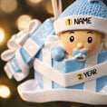 Load image into Gallery viewer, Personalized Baby Boy First Christmas Ornament featuring an adorable baby popping out of a blue gift box with a matching hat and pacifier. The name is displayed on the hat while the year is placed on the ribbon detail, with Baby’s 1st Christmas written along the base. Soft blue and white tones, raised 3D elements, and sweet holiday details make this a charming keepsake. Perfect for newborn boys, baby showers, and celebrating a baby’s very first Christmas season.