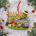 Load image into Gallery viewer, Personalized gardener ornament featuring a detailed garden scene with wooden fence wheelbarrow potted plants gardening tools and soil elements. The design includes a customizable name on the fence and a year on the base making it a thoughtful keepsake for garden lovers. The ornament has a warm rustic farmhouse style and is displayed with a red hanging ribbon suitable for Christmas trees seasonal decor and gift displays.