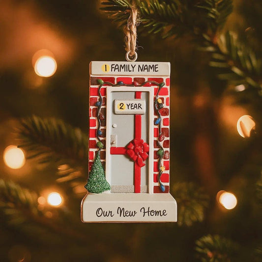 Decorative ornament with a door design, family name placeholder, and 'Our New Home' text, hanging on a Christmas tree.