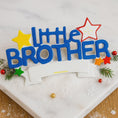Load image into Gallery viewer, Colorful 'Little Brother' decoration on a white surface with stars and greenery.
