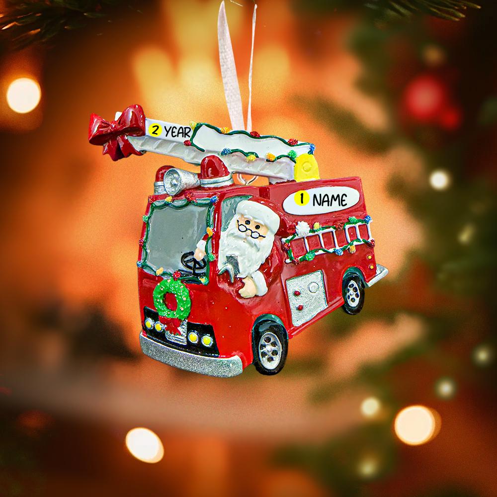 Christmas ornament of a red fire truck with Santa driving, against a blurred Christmas tree background.