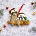 Load image into Gallery viewer, Christmas ornament with two sloths on a log, each wearing a Santa hat, on a snowy background.
