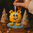 Load image into Gallery viewer, Yellow cartoon-like creature ornament with a hand holding it against a festive background.
