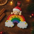 Load image into Gallery viewer, Decorative ornament with a rainbow, clouds, and a baby figure on a wooden surface.
