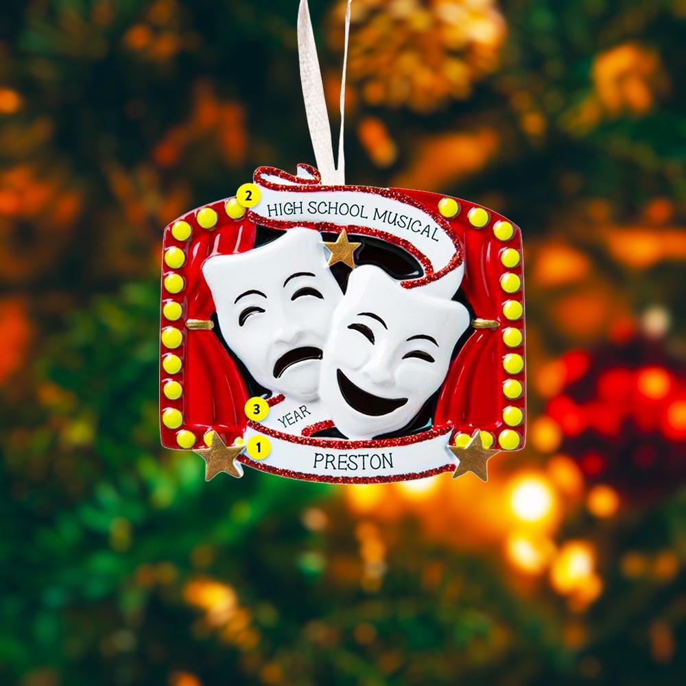 Decorative ornament with theater masks and text on a blurred Christmas tree background