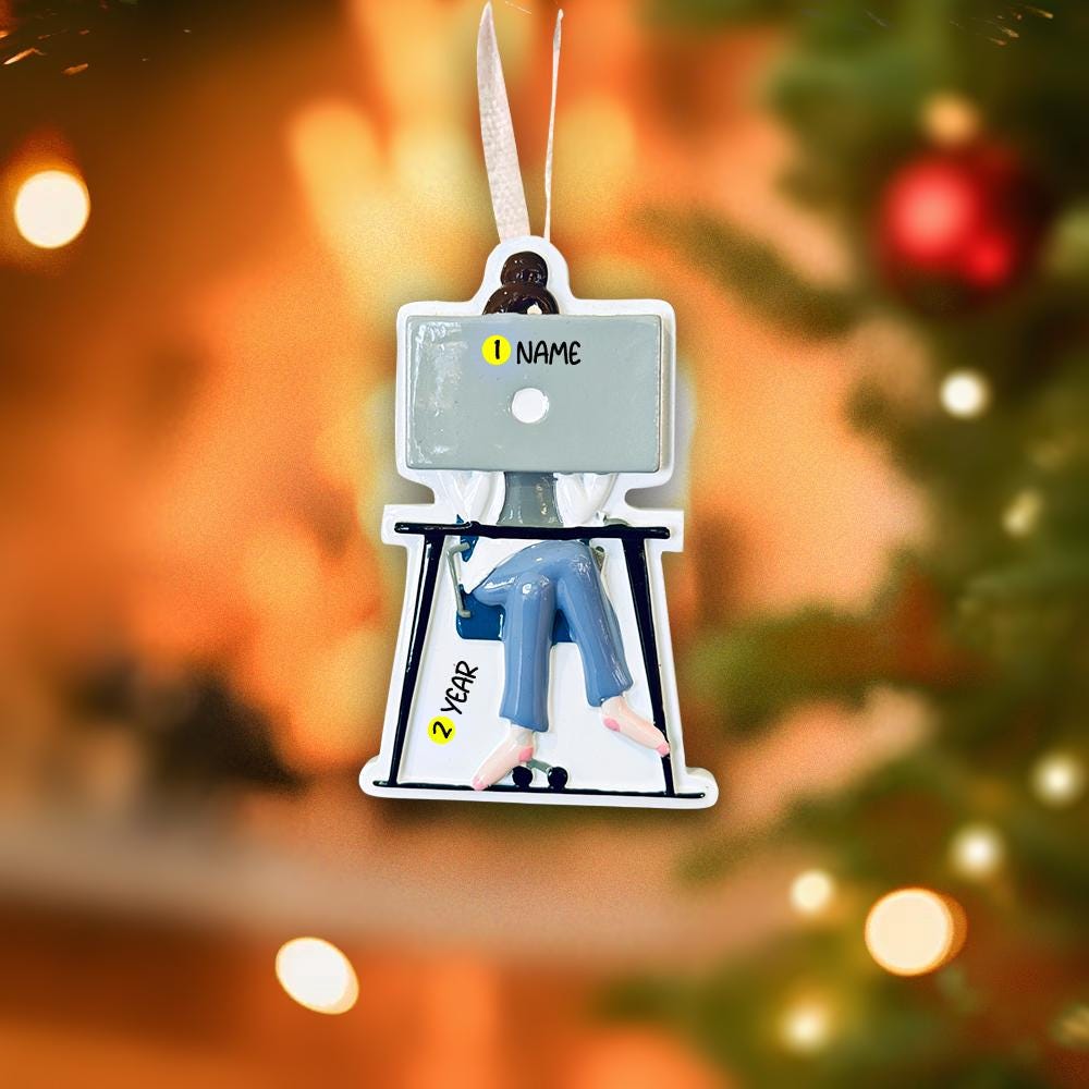 Decorative ornament with a person sitting at a desk, resembling a screen, against a blurred Christmas tree background.