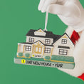 Load image into Gallery viewer, House-shaped ornament with 'Our New House + Year' text held by a gloved hand against a green background
