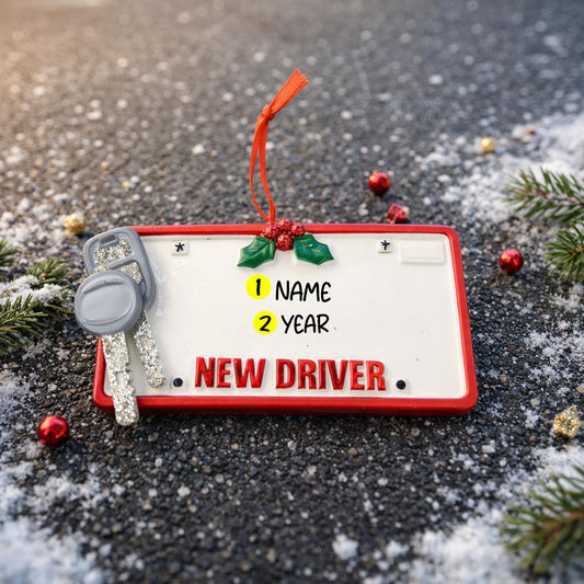 Decorative ornament resembling a 'New Driver' license plate with a key and holly decorations on a snowy background.