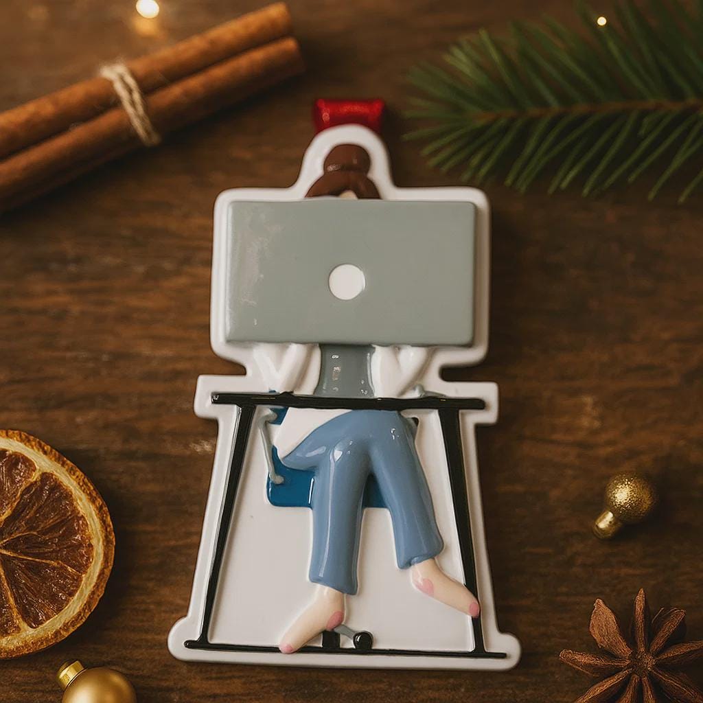 Decorative figurine of a person sitting on a chair with a laptop, surrounded by Christmas decorations on a wooden surface.