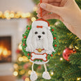 Load image into Gallery viewer, Maltese Dog-shaped Christmas ornament with a wreath and Santa hat held in front of a decorated Christmas tree.
