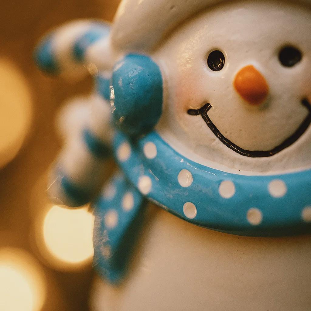 Close-up of a snowman figurine with a blue scarf against a blurred light background