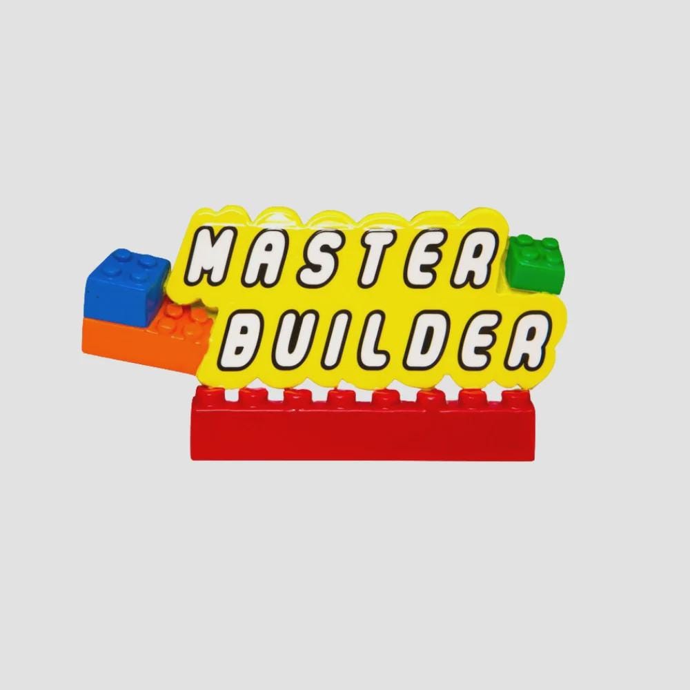 Personalized Master Builder Christmas ornament featuring a raised 3D front with colorful building block design and bold lettering. The ornament has a flat 2D back for easy hanging and durability. Bright primary colors and playful block details make it perfect for kids who love building toys. Personalization includes name and year, added by hand, making it a fun and meaningful holiday keepsake for children and young builders.