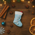 Load image into Gallery viewer, A glossy resin baby boy stocking ornament features a soft pastel blue Christmas stocking shape with a raised glitter style baby figure on the front, white cuff detail, small star accents, and smooth painted surfaces, surrounded by warm holiday lights and nursery themed props, handwritten personalization showing one baby name on the top cuff and the year written near the bottom of the stocking, designed as a mostly 2D ornament with raised 3D details on the front only.
