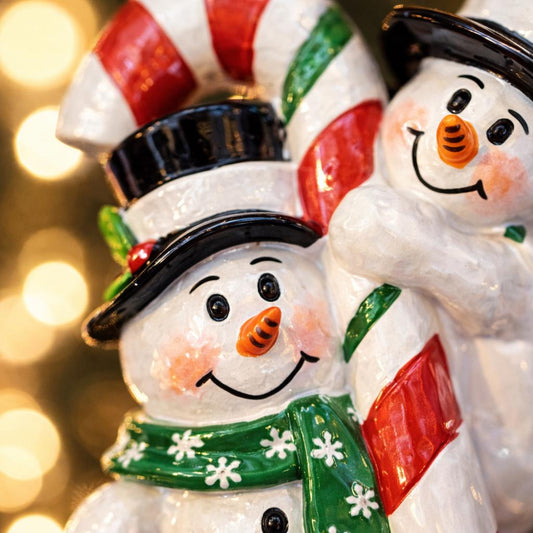 Two snowman figurines with candy cane hats against a blurred light background
