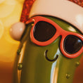 Load image into Gallery viewer, Green character with red sunglasses and a Santa hat on a colorful background

