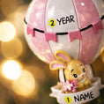 Load image into Gallery viewer, A personalized baby girl ornament featuring a cute bunny riding a pastel pink hot air balloon. Soft pink and white tones with delicate bow details create a sweet and cozy look. Handwritten personalization includes baby name and year. Mostly 2D ornament with raised 3D details on the front only, lightweight and easy to hang, perfect for baby first Christmas, nursery decor, and toddler keepsakes.
