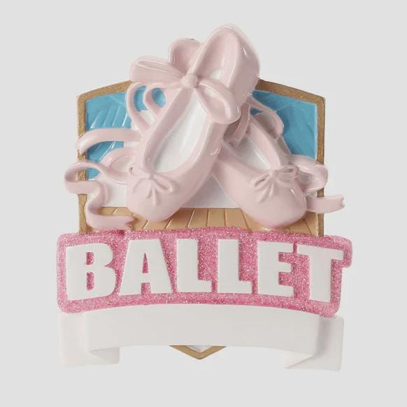 Personalized ballet Christmas ornament featuring soft pink ballet shoes with delicate ribbon details and a glittered ballet banner, customizable name area on the lower front ribbon and customizable year area beside the name, glossy finish with raised 3D front elements and flat 2D back, white hanging ribbon, displayed on a warm snowy holiday background with festive greenery ornaments and cozy Christmas decor.