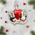 Load image into Gallery viewer, Personalized Christmas ornament with two penguins holding a heart, surrounded by festive decorations on a snowy background.
