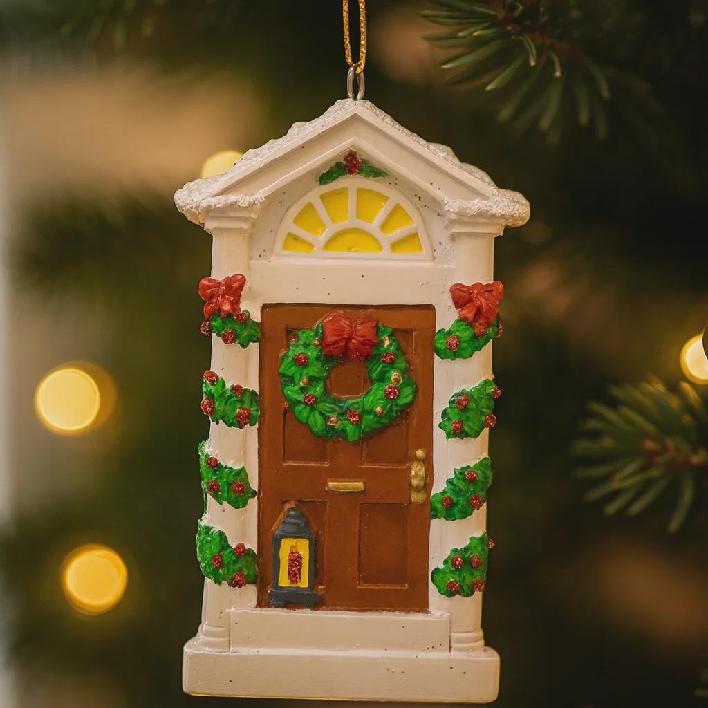 Decorative Christmas ornament of a house with a wreath on a blurred Christmas tree background.